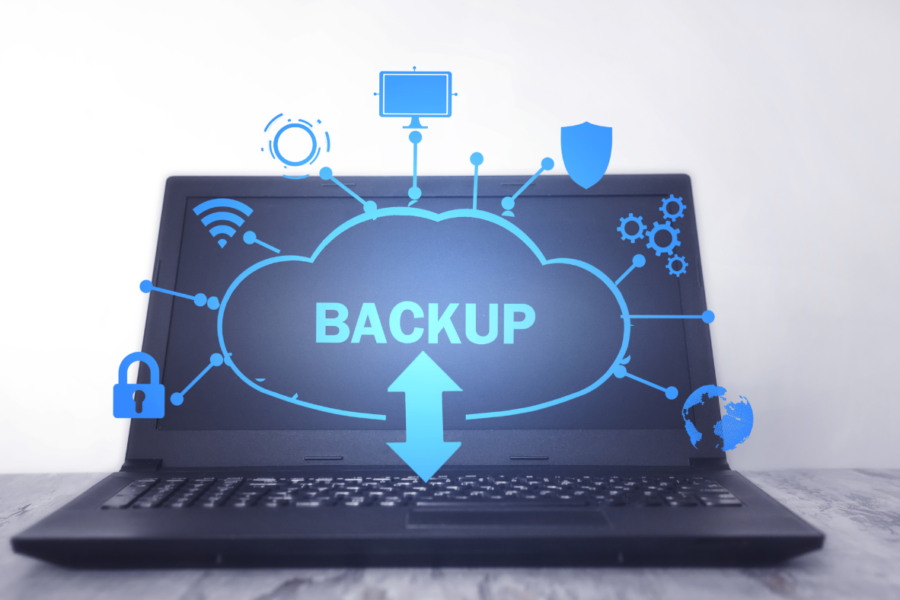 An open laptop on a table. On the screen a cloud with the word 'backup' is popping off the screen along with icons for wifi, security, automation and more.
