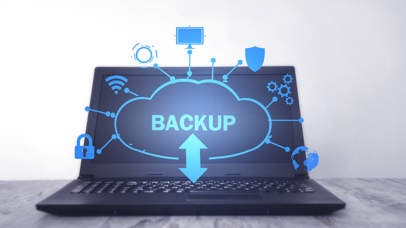 An open laptop on a table. On the screen a cloud with the word 'backup' is popping off the screen along with icons for wifi, security, automation and more.