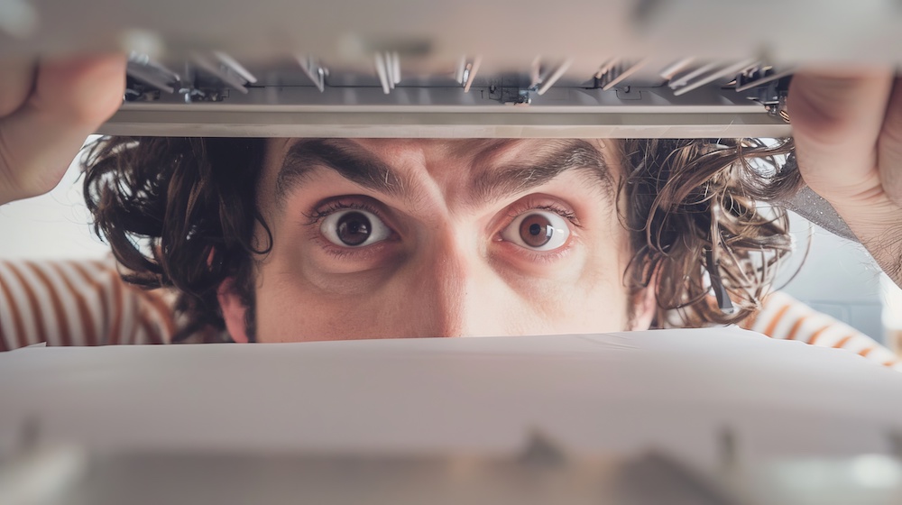 A person peering into an open business printer, trying to remove a jammed piece of paper