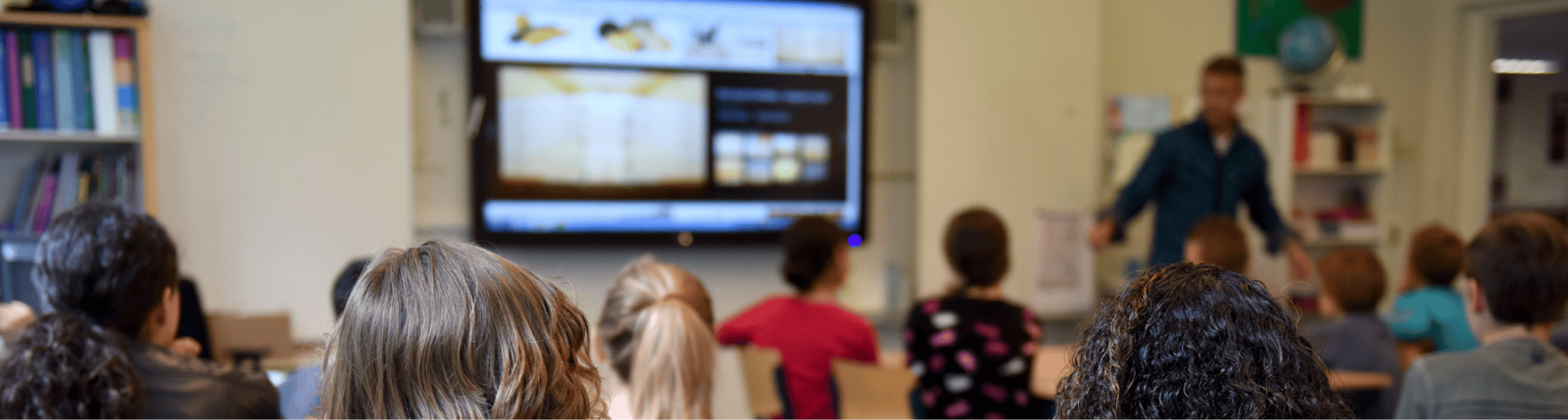 A classroom full of students with a teacher in the front of the classroom using a smartboard to share an interactive lesson.