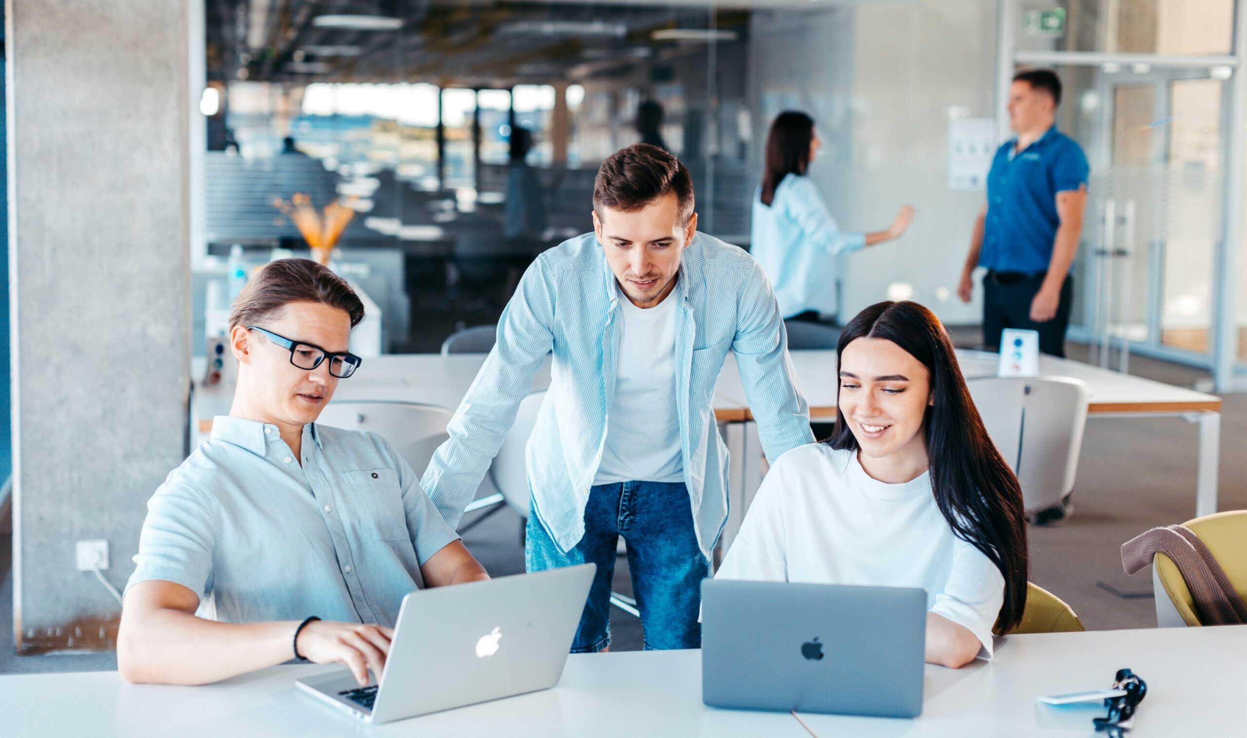 Two IT team members work on laptops while an IT service provider stands beside them, offering support and guidance.