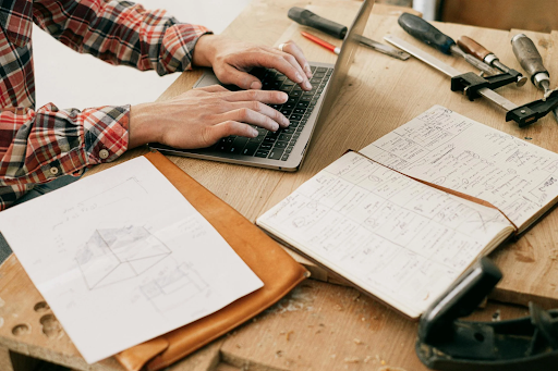 A construction worker uses a laptop to digitize project plans and manage documentation. Source: https://www.pexels.com/photo/person-using-macbook-pro-on-brown-wooden-table-4491910/