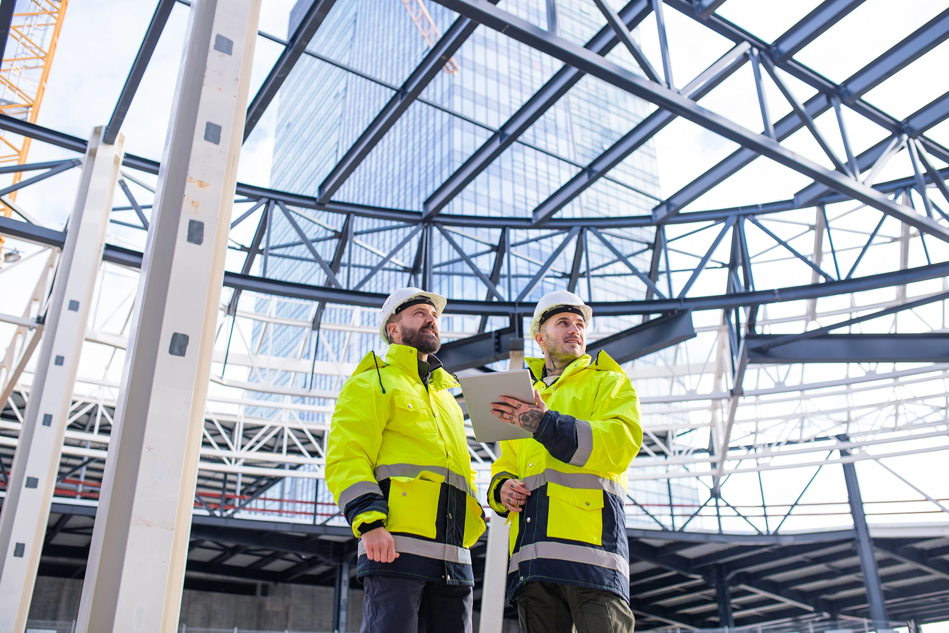 Two construction professionals in high-visibility gear review project data on a tablet at a commercial jobsite, highlighting the use of business process automation tools in the construction industry.