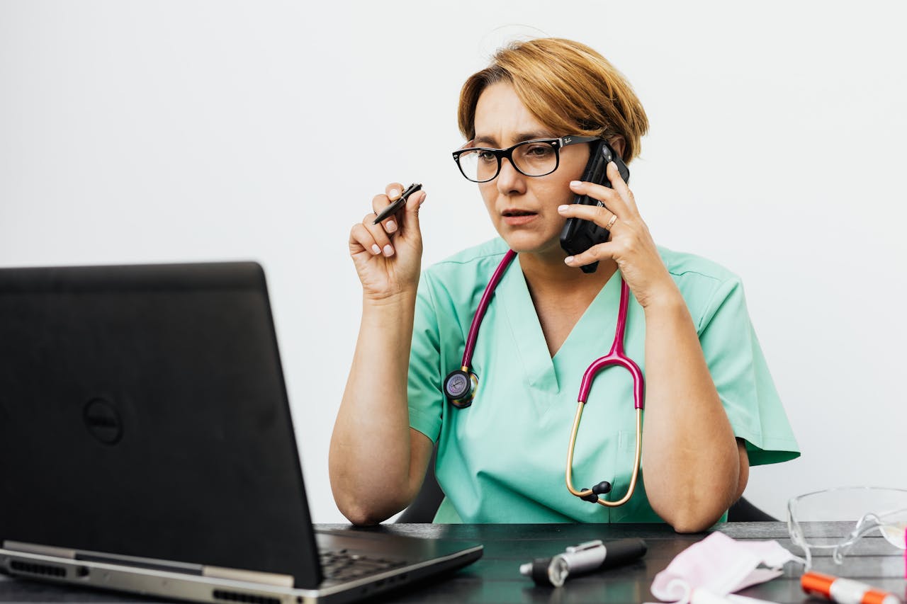 A healthcare professional consults over the phone while using a laptop, highlighting the importance of strong cybersecurity measures.