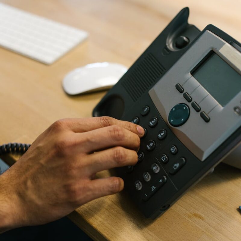 Person dialing a VoIP office phone, demonstrating modern internet-based business communication.