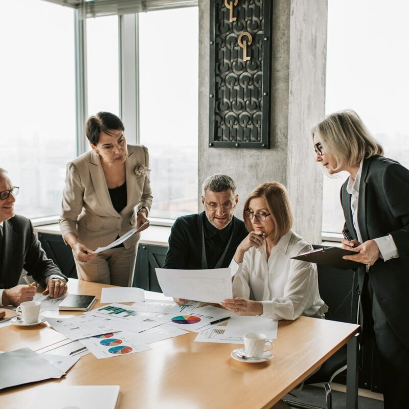 A group of business professionals, reviewing documents and data charts as part of a comprehensive cyber risk assessment meeting.
