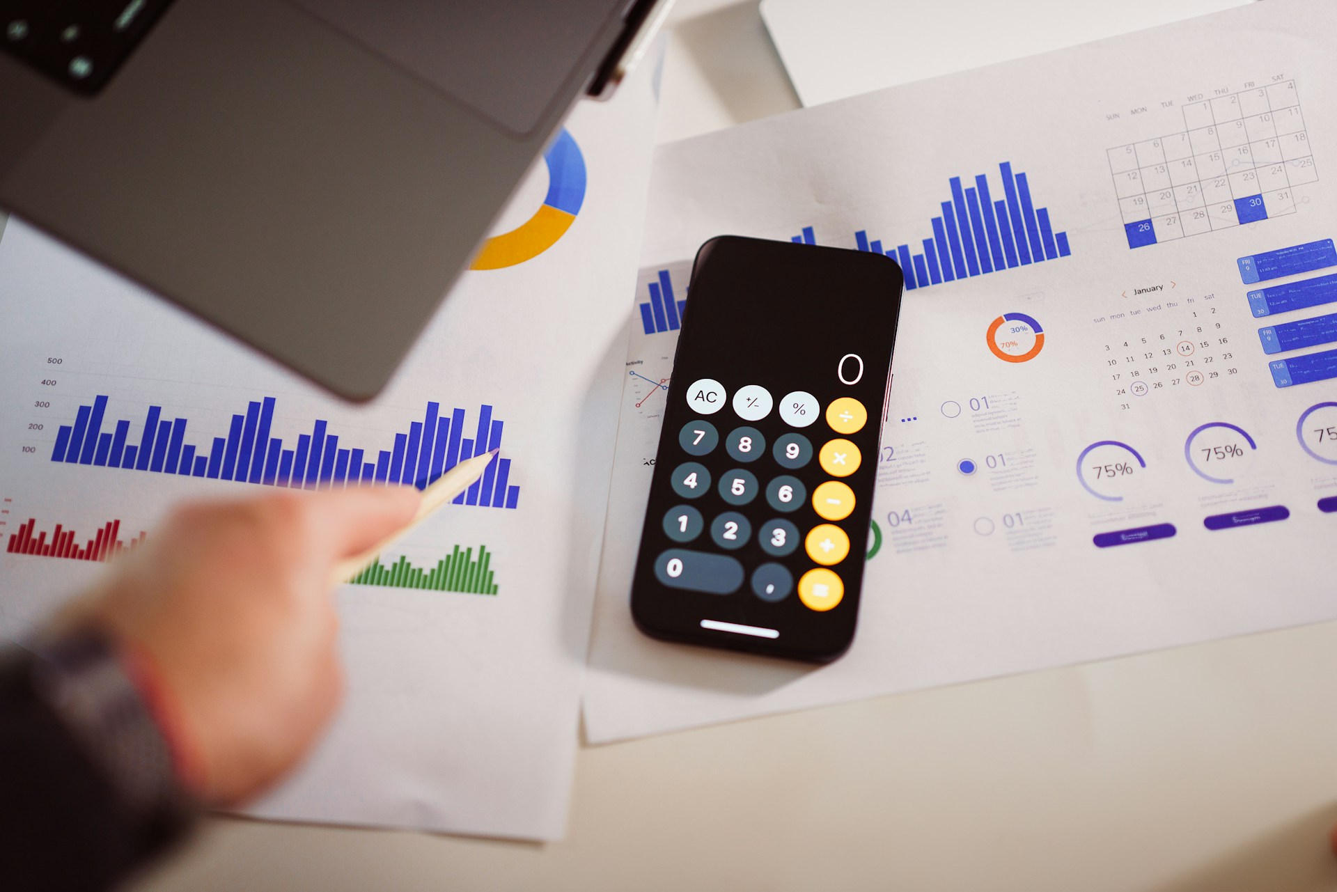 Person points to a bar graph next to a calculator and charts, analyzing data for a cybersecurity budget.