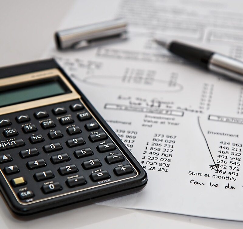 A calculator, pen, and financial report with handwritten notes suggest a business evaluating costs and coverage options for cyber insurance.