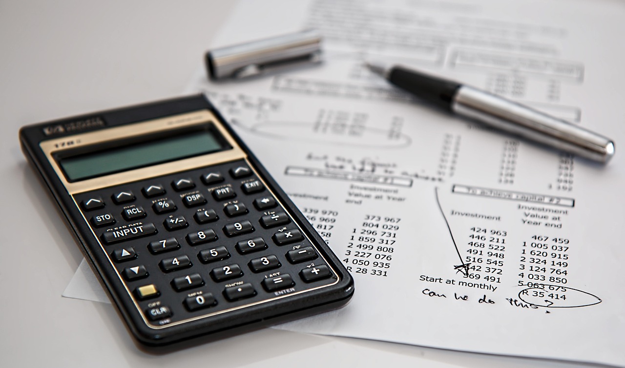 A calculator, pen, and financial report with handwritten notes suggest a business evaluating costs and coverage options for cyber insurance.