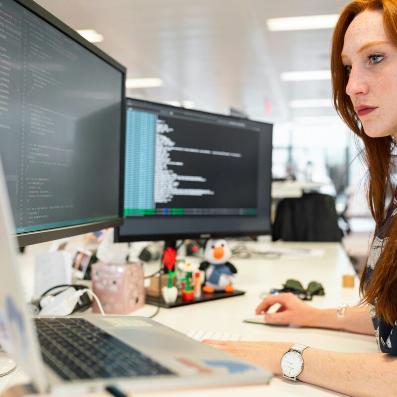 A professional analyzing and coding on multiple monitors, emphasizing the importance of cybersecurity and tech expertise for business leaders.