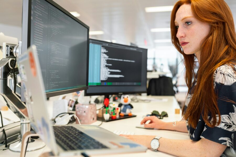 A professional analyzing and coding on multiple monitors, emphasizing the importance of cybersecurity and tech expertise for business leaders.
