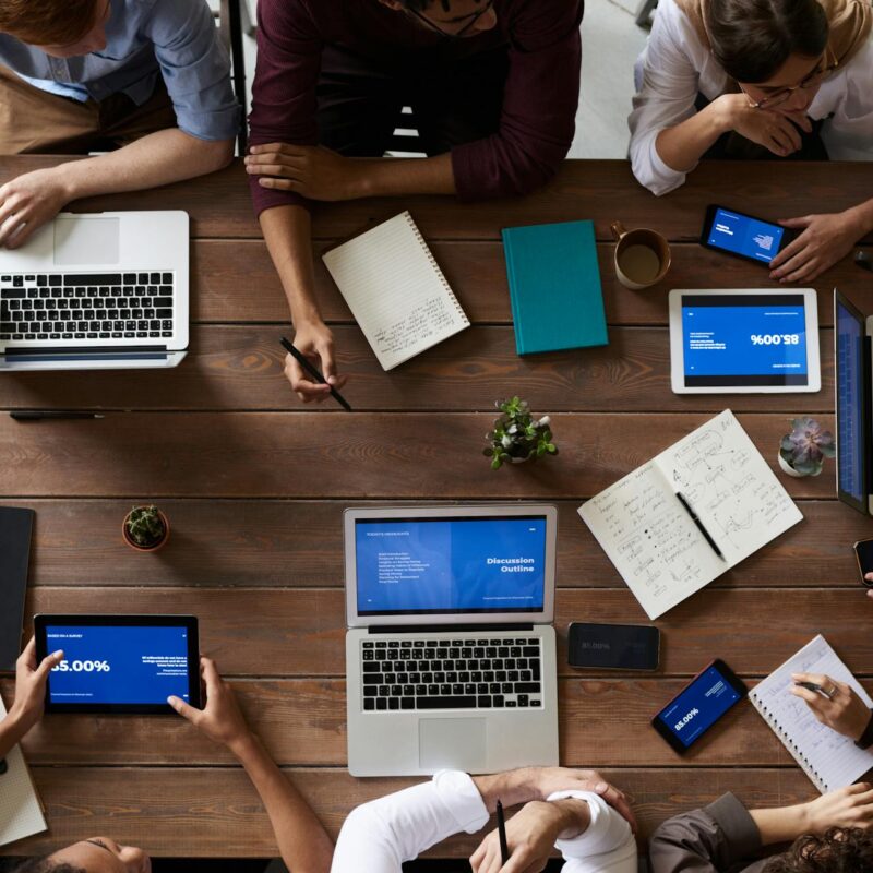 Team collaborating on cloud software development using laptops, tablets, and smartphones around a table.