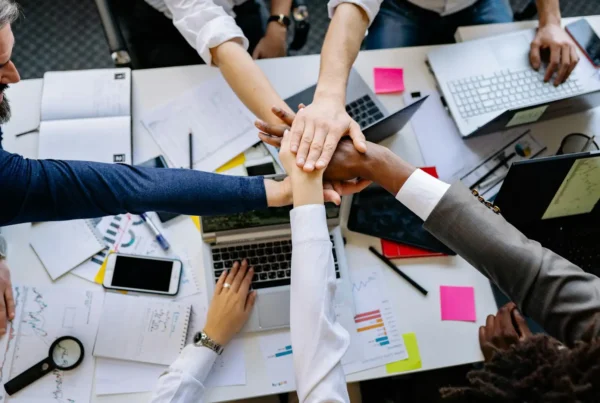 A team collaborates around laptops and documents, using AI tools to improve teamwork and efficiency.