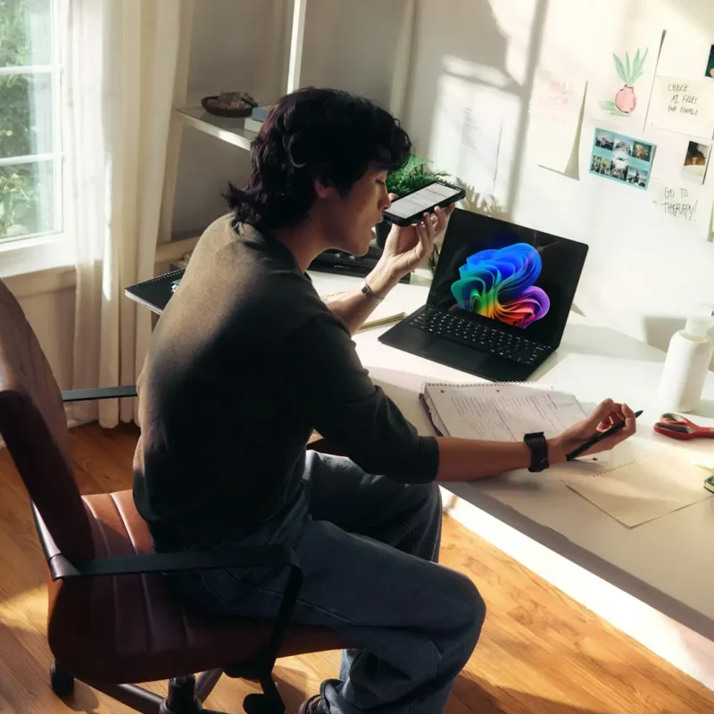 Person working at a desk using AI Copilot on a laptop while referencing notes and a smartphone for AI-assisted decision-making.