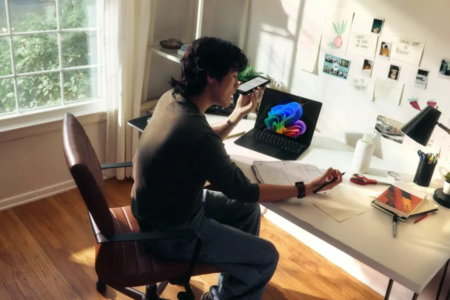 Person working at a desk using AI Copilot on a laptop while referencing notes and a smartphone for AI-assisted decision-making.