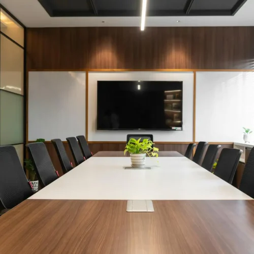 Modern conference meeting room setup with a long boardroom table, ergonomic chairs, and a wall-mounted presentation screen.