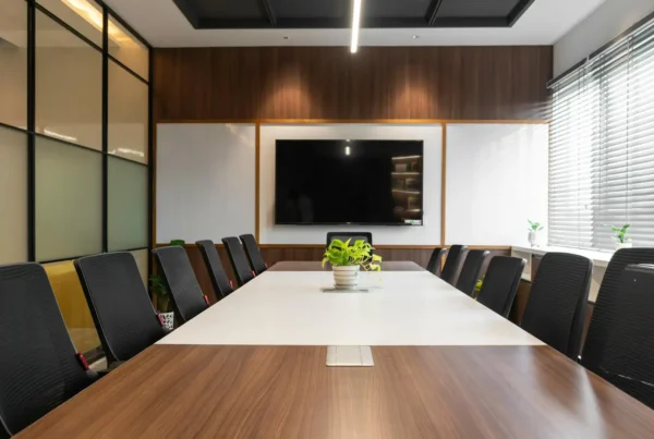 Modern conference meeting room setup with a long boardroom table, ergonomic chairs, and a wall-mounted presentation screen.