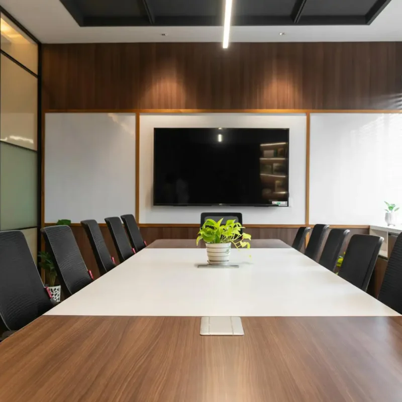 Modern conference meeting room setup with a long boardroom table, ergonomic chairs, and a wall-mounted presentation screen.