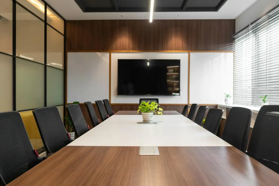 Modern conference meeting room setup with a long boardroom table, ergonomic chairs, and a wall-mounted presentation screen.