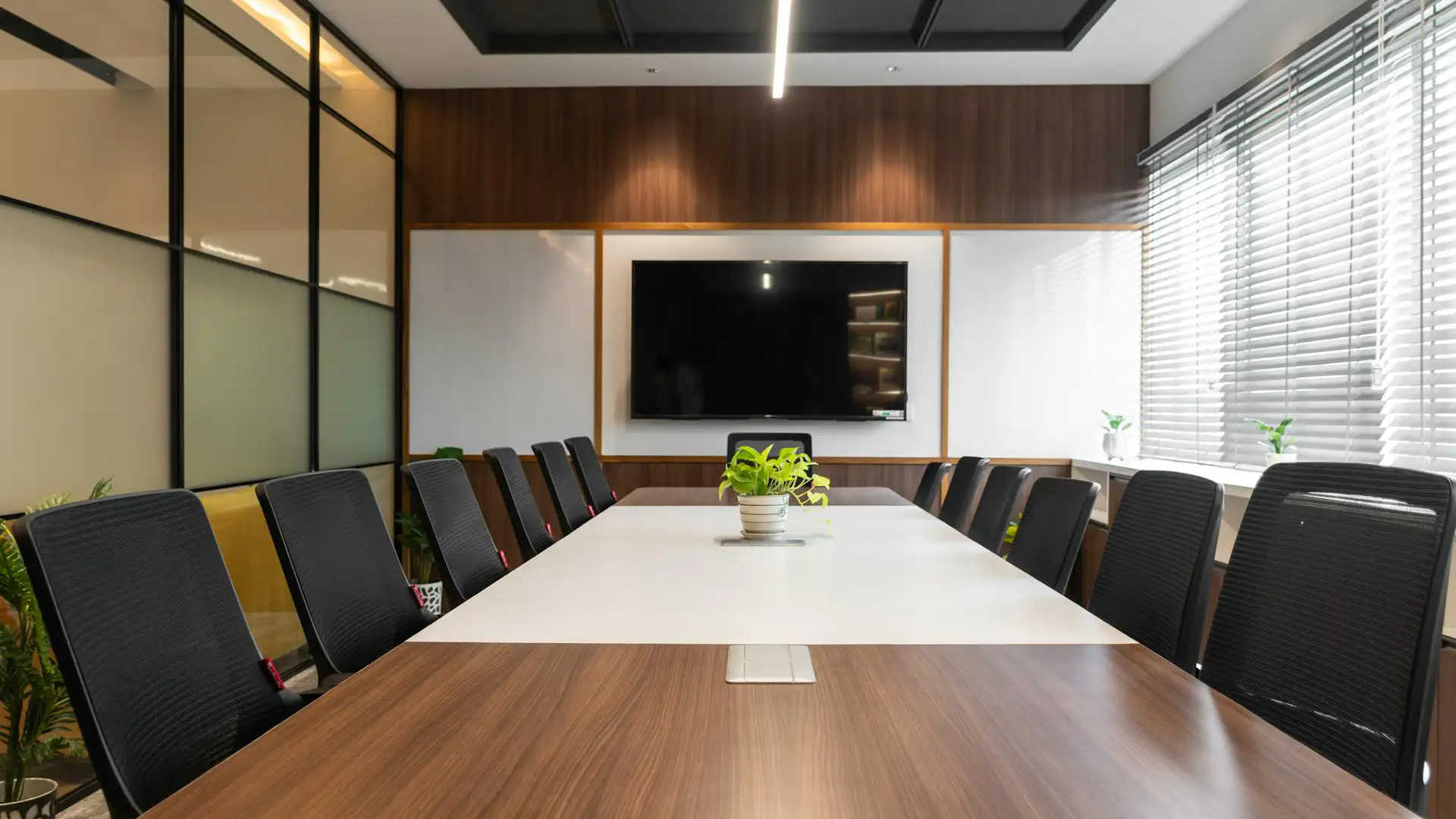 Modern conference meeting room setup with a long boardroom table, ergonomic chairs, and a wall-mounted presentation screen.