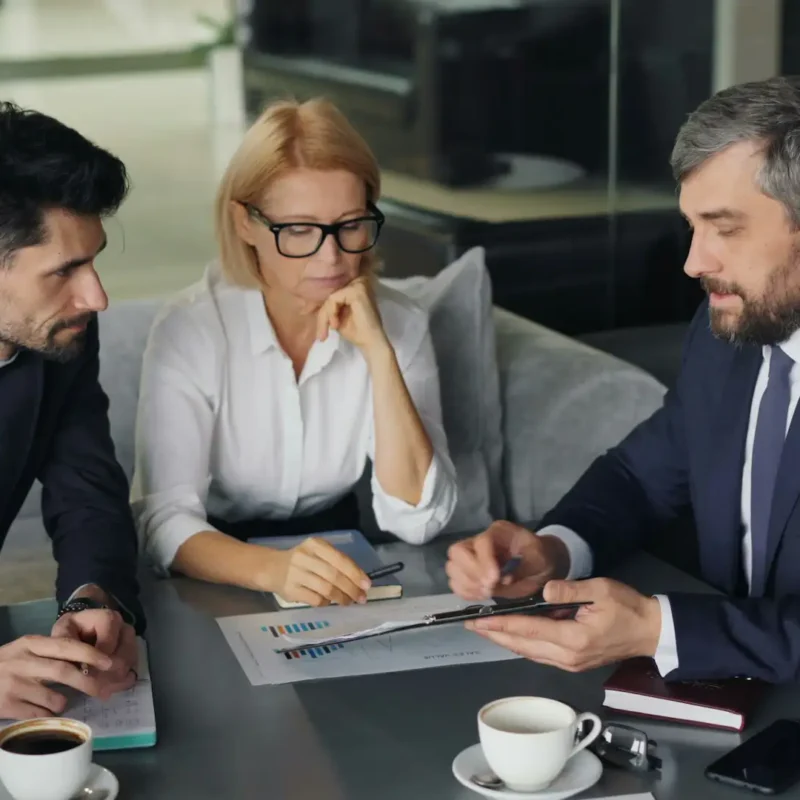 An IT provider consultant reviews documents and data reports during a business meeting with clients.