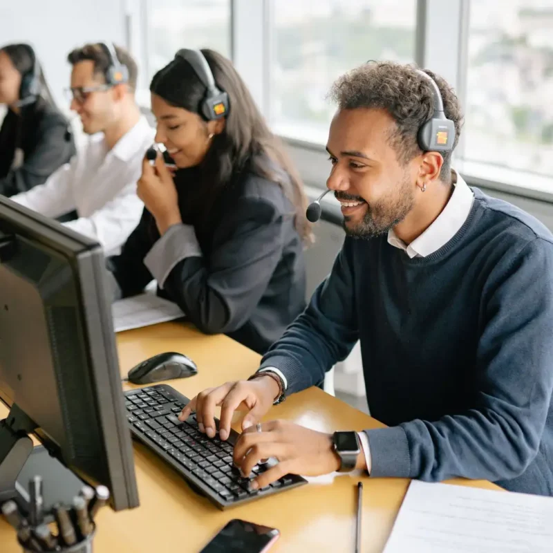 A team of agents wearing headsets and working on computers at a row of desks in a contact center.