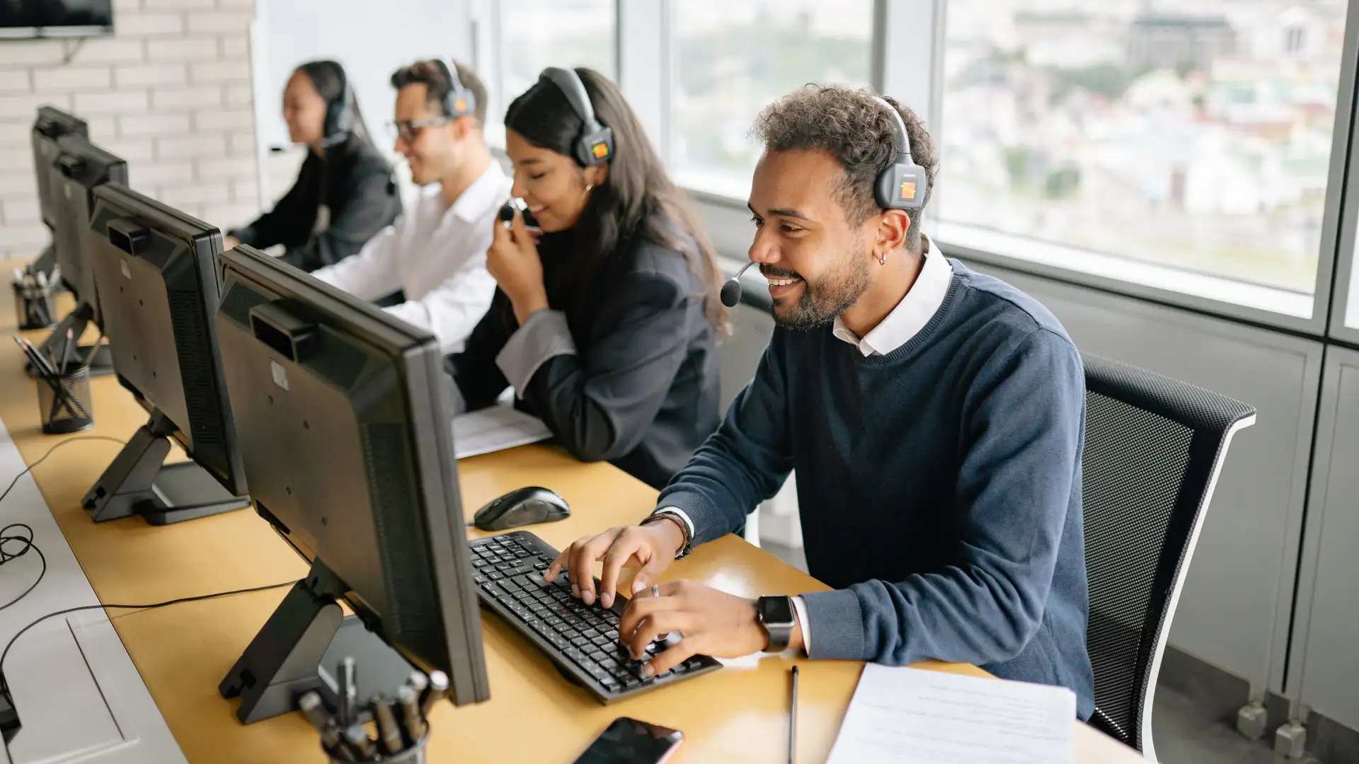 A team of agents wearing headsets and working on computers at a row of desks in a contact center.