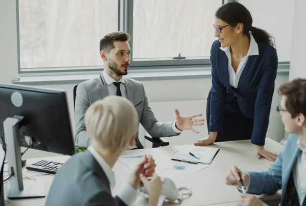 A professional team discussing IT audit findings and strategy around a desk with computer monitors and documents