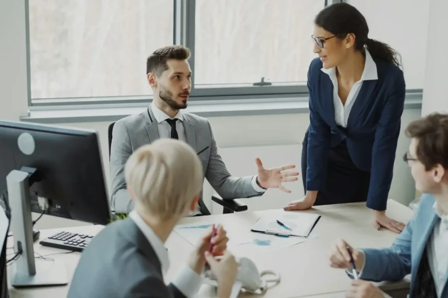 A professional team discussing IT audit findings and strategy around a desk with computer monitors and documents