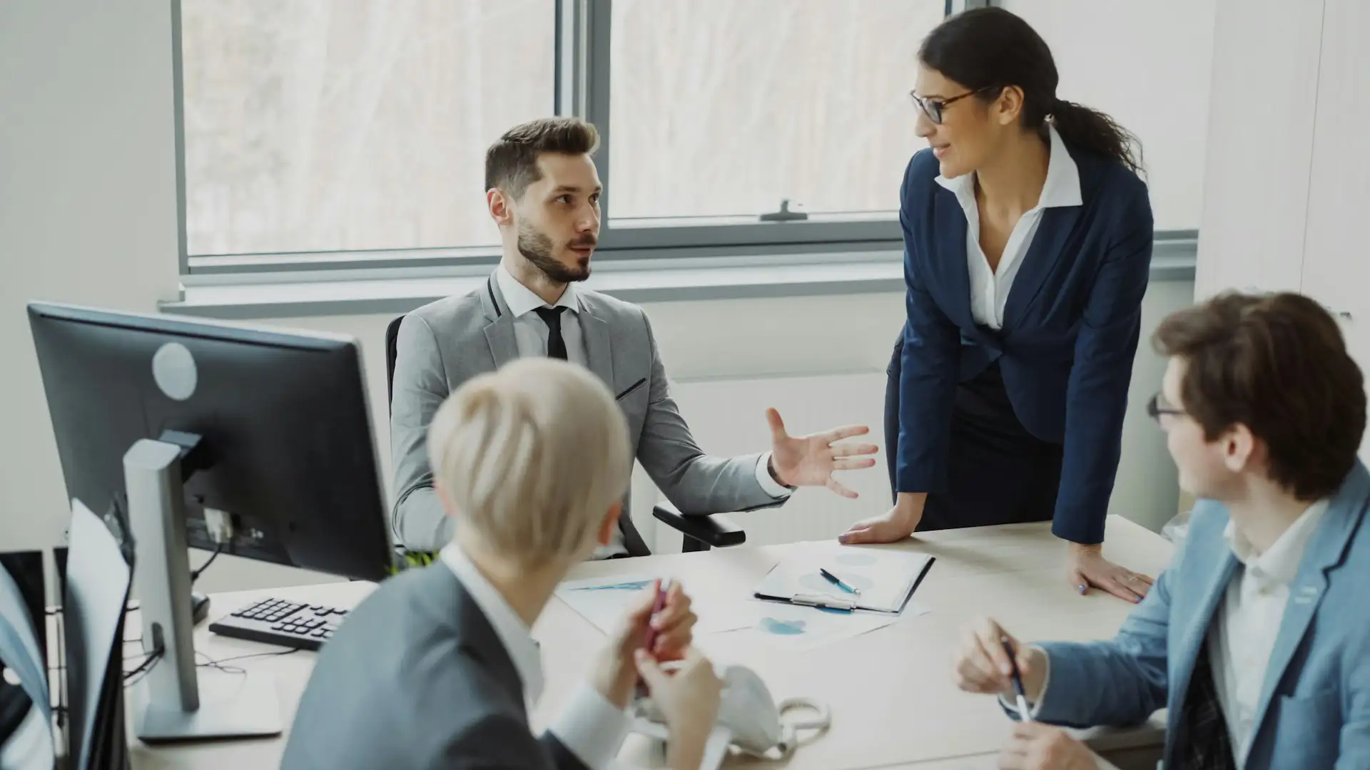 A professional team discussing IT audit findings and strategy around a desk with computer monitors and documents